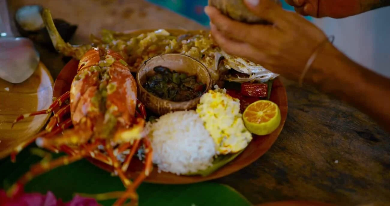 Lobster and seafood platter with rice, lemon, and dipping sauce on a wooden table.